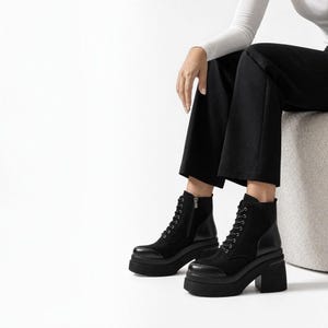 May include: Black ankle boots featuring a lace-up front, a side zipper, and a thick platform sole with a block heel. The boots are constructed with a combination of smooth leather and suede-like panels, providing a textured appearance.