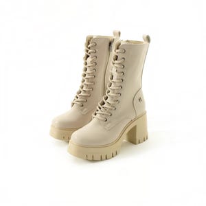 May include: A pair of cream-colored mid-calf boots featuring a lace-up front with matching laces, a side zipper closure, a thick platform sole, and a chunky block heel. The boots have a smooth finish and a small metallic logo on the outer side.
