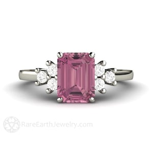 May include: A silver ring with a pink emerald-cut gemstone surrounded by smaller diamonds.