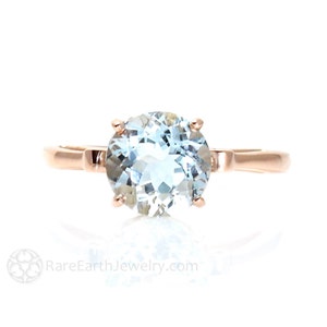 K&ouml;nnte beinhalten: Ein Ring aus Ros&eacute;gold mit einem gro&szlig;en, runden, hellblauen Aquamarin-Edelstein. Der Ring hat ein schlichtes Band und eine vierzackige Fassung.