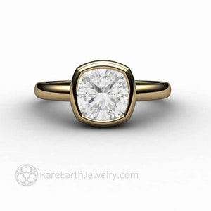 May include: A gold ring featuring a large, square-shaped, bezel-set diamond. The diamond has a cushion cut and is surrounded by a thin gold band.