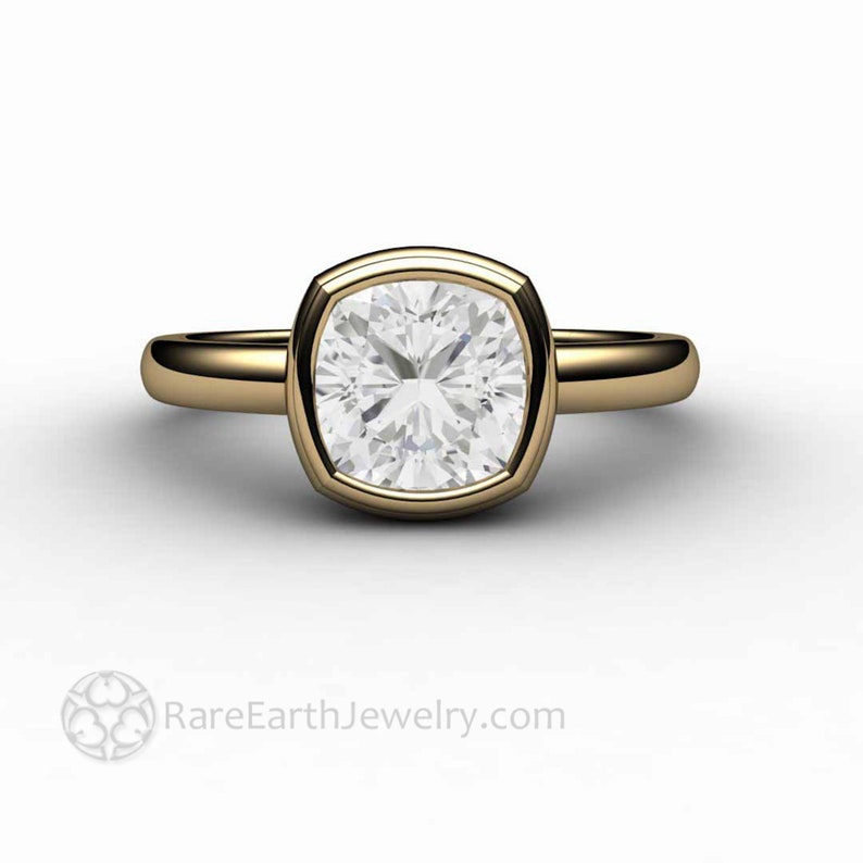 May include: A gold ring featuring a large, square-shaped, bezel-set diamond. The diamond has a cushion cut and is surrounded by a thin gold band.