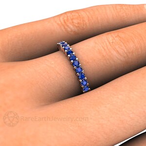 May include: A delicate eternity band featuring a row of round blue sapphires set in a white metal band. RareEarthJewelry.com