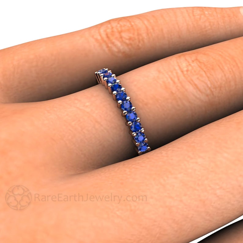 May include: A delicate eternity band featuring a row of round blue sapphires set in a white metal band. RareEarthJewelry.com