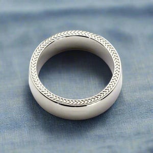 Puede incluir: Un anillo de plata con un diseño trenzado alrededor del borde.