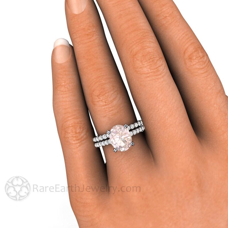 Op de afbeelding: Een close-up van een vrouwenhand met een zilveren ovale verlovingsring met een middelste steen en een bijpassende trouwring. De ring is bezet met kleine diamanten rond de middelste steen en de band.