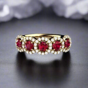 May include: A gold band ring featuring five red ruby gemstones, each encircled by a halo of smaller diamonds.
