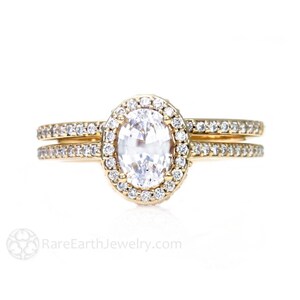 May include: A gold engagement ring set with a large oval-shaped center stone surrounded by a halo of smaller diamonds. The band is also set with smaller diamonds.