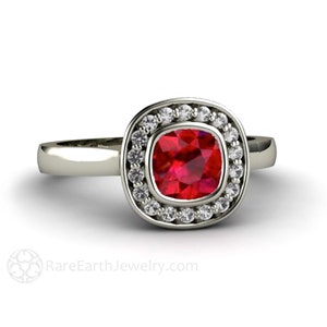 May include: A silver ring with a red gemstone surrounded by a halo of smaller white gemstones.