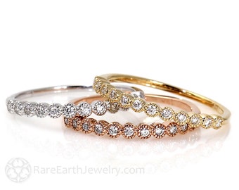 May include: Three delicate stacking rings with bezel-set round diamonds. The rings are in white gold, yellow gold, and rose gold.