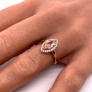 May include: A rose gold engagement ring with a marquise cut morganite center stone and a halo of smaller diamonds.