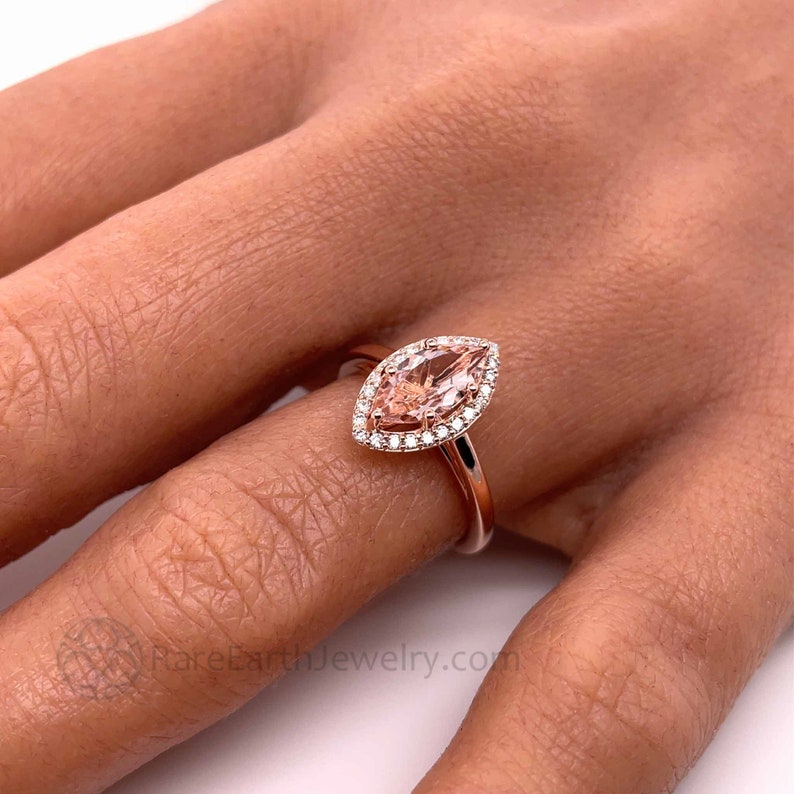 May include: A rose gold engagement ring with a marquise cut morganite center stone and a halo of smaller diamonds.