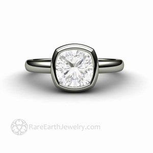 May include: A silver ring featuring a large, cushion-cut diamond set in a bezel setting. The ring has a plain band and a polished finish.