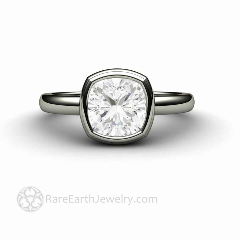 May include: A silver ring featuring a large, cushion-cut diamond set in a bezel setting. The ring has a plain band and a polished finish.