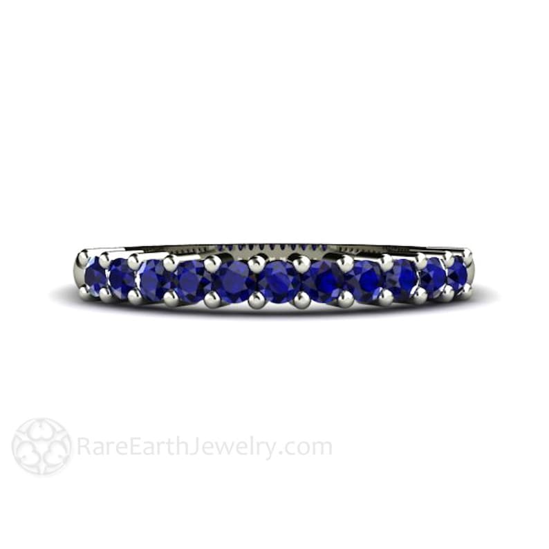 May include: A delicate silver band with a row of round blue sapphires. The band is set with a total of nine sapphires.