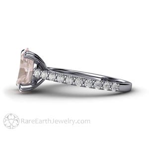 Op de afbeelding: Een delicate verlovingsring met een lichtroze vierkante edelsteen omgeven door een halo van kleinere diamanten. De band is bezet met een rij kleinere diamanten.