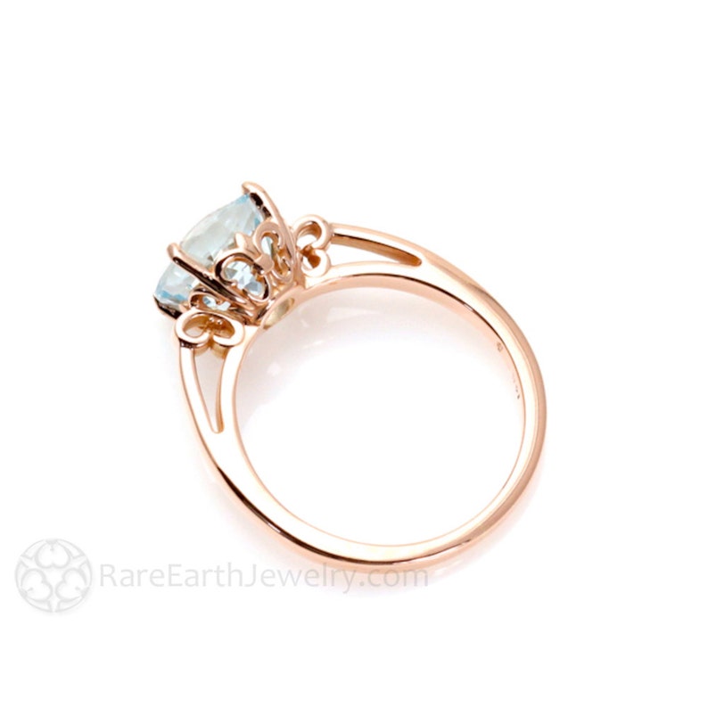 K&ouml;nnte beinhalten: Ein Ring aus Ros&eacute;gold mit einem hellblauen Edelstein, der in einem filigranen, verzierten Design gefasst ist. Der Ring hat ein florales Motiv mit filigranen Details.