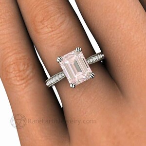 May include: A delicate engagement ring with a large, pale pink, emerald-cut gemstone surrounded by a band of smaller, sparkling diamonds.
