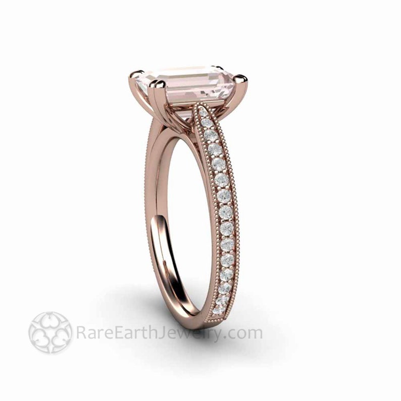 May include: A rose gold engagement ring with a large, emerald-cut, pale pink gemstone. The band is set with a row of smaller, round, white gemstones.