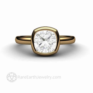 May include: A gold engagement ring featuring a large, square-shaped diamond set in a bezel.