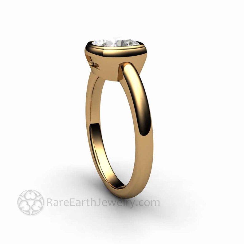 May include: A gold ring with a bezel setting featuring a round, clear gemstone. The ring has a simple band.