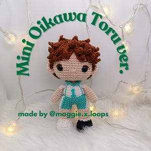 May include: A crocheted amigurumi doll of Oikawa Tooru from the anime Haikyuu!! The doll is wearing a white and teal volleyball uniform with the number 1 on the front. The doll has brown hair and a friendly expression.