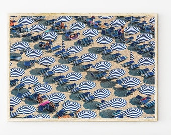 Könnte beinhalten: Eine Luftaufnahme eines Strandes mit blau-weiß gestreiften Sonnenschirmen und Liegestühlen. Die Sonnenschirme sind in einem Gittermuster angeordnet, wodurch ein geometrisches Design entsteht.