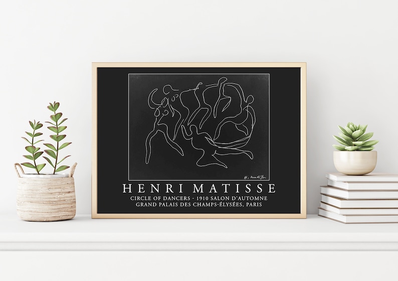 May include: Black and white line art print of Henri Matisse's "Circle of Dancers" artwork. The print features a single continuous line drawing of dancers in a circle. The print is framed in a light wood frame and has the title "Henri Matisse" and "Circle of Dancers - 1910 Salon d'Automne Grand Palais des Champs-&Eacute;lys&eacute;es, Paris" printed below the artwork.