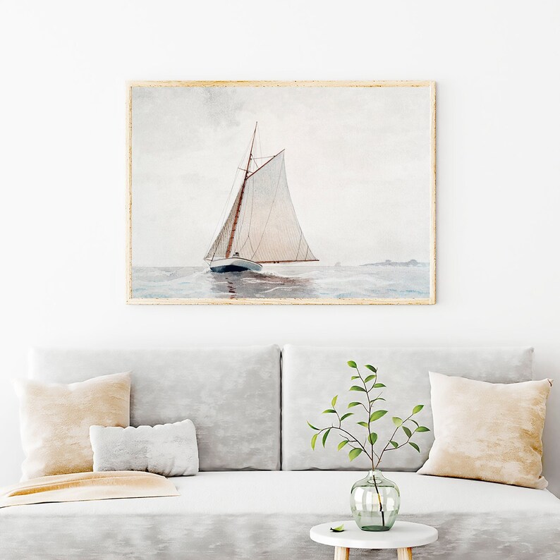 Puede incluir: Una pintura de acuarela de un velero con velas blancas en un mar tranquilo y gris. El velero navega lejos del espectador, con la proa del barco mirando hacia el lado izquierdo de la imagen. La pintura est&aacute; enmarcada en un marco de madera claro.