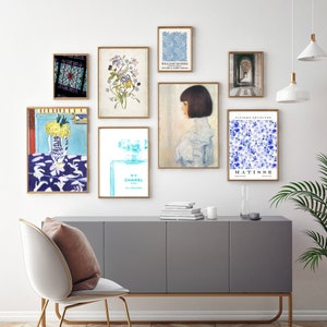 May include: A gallery wall with nine framed prints. The prints feature a variety of subjects, including a stained glass window, flowers, a perfume bottle, a portrait of a woman, and abstract art. The prints are arranged in a grid pattern on a white wall.