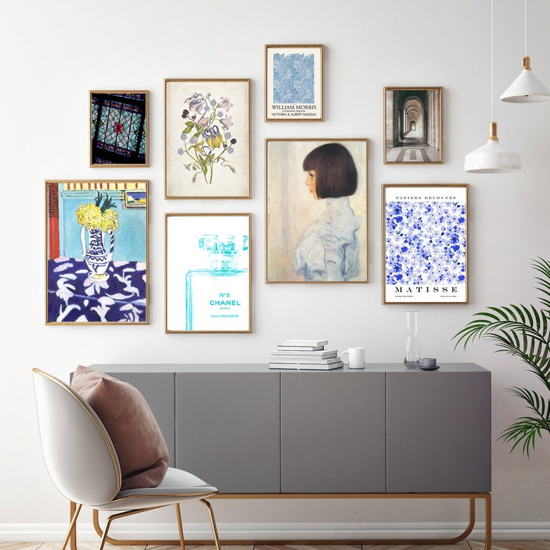May include: A gallery wall with nine framed prints. The prints feature a variety of subjects, including a stained glass window, flowers, a perfume bottle, a portrait of a woman, and abstract art. The prints are arranged in a grid pattern on a white wall.