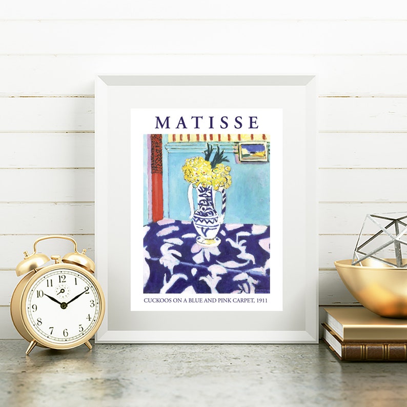 May include: A framed print of a painting by Henri Matisse titled "Cuckoos on a Blue and Pink Carpet, 1911". The painting depicts a vase of yellow flowers on a table with a blue and pink patterned tablecloth.