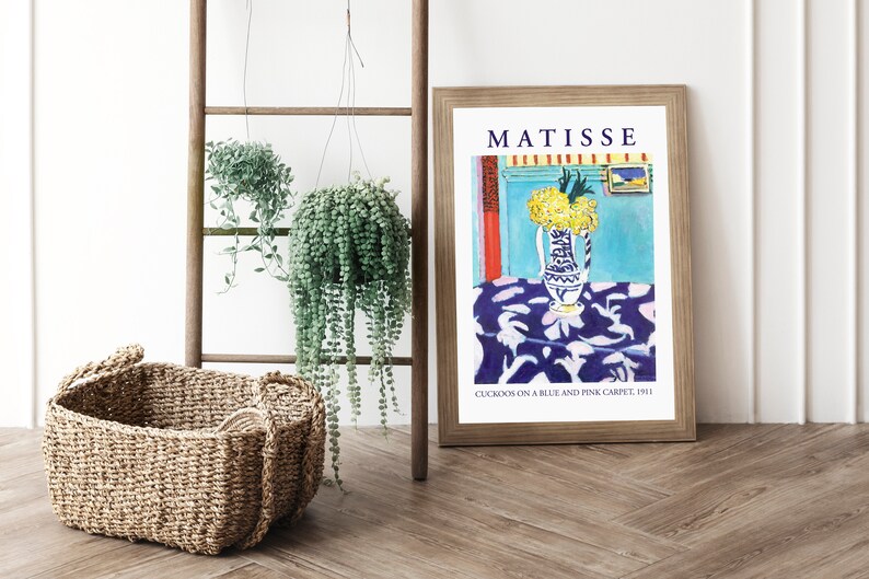 May include: A framed print of a painting by Henri Matisse titled "Cuckoos on a Blue and Pink Carpet, 1911". The painting depicts a vase of yellow flowers on a blue tablecloth with a white and pink pattern.