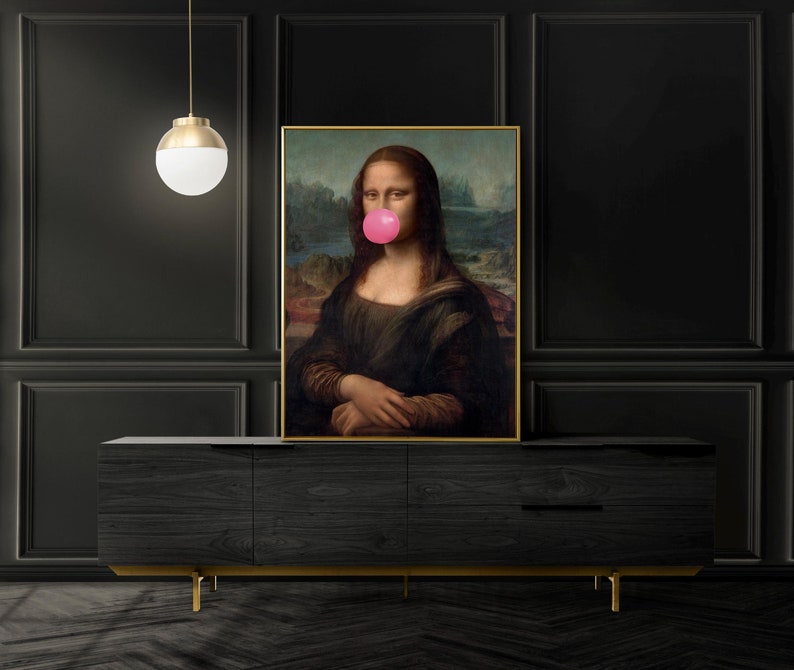 May include: A framed print of the Mona Lisa with a pink bubble gum stuck to her mouth. The print is hanging on a black wall above a dark wood cabinet.