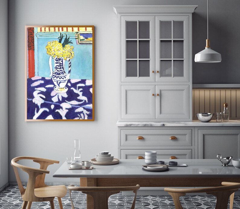 May include: A painting of a still life featuring a blue and white vase filled with yellow flowers on a blue and white patterned tablecloth. The painting is framed in a brown frame and is hanging on a light blue wall.