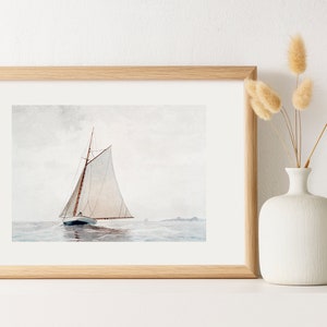 Puede incluir: Una pintura de acuarela enmarcada de un velero con velas blancas en un mar tranquilo. La pintura est&aacute; en un marco de madera claro y est&aacute; colgada en una pared blanca.