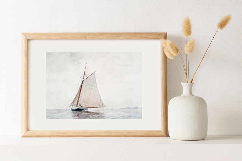 Puede incluir: Una pintura de acuarela enmarcada de un velero con velas blancas en un mar tranquilo. La pintura est&aacute; en un marco de madera claro y est&aacute; colgada en una pared blanca.