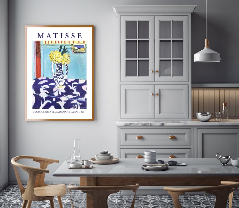 May include: A framed print of a painting by Henri Matisse titled "Cuckoos on a Blue and Pink Carpet, 1911". The painting depicts a vase of yellow flowers on a blue and pink patterned tablecloth.