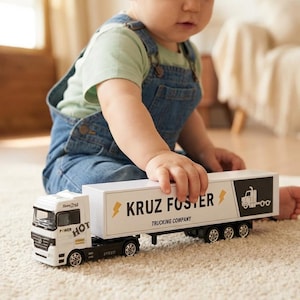 Könnte beinhalten: Ein weißer und schwarzer Spielzeug-LKW mit dem Text "KRUZ FOSTER TRUCKING COMPANY" und einer Blitzgrafik. Der LKW hat einen Anhänger und steht auf einem Teppich. Auf der Kabine steht das Wort "HOT".