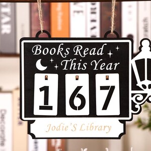 Könnte beinhalten: Schwarz-weißes Holzschild mit der Aufschrift "Books Read This Year" und der Zahl "167". Das Schild hat ein dekoratives Straßenlampen-Design und ist mit "Jodie's Library" personalisiert. Zum Lesen von Büchern.