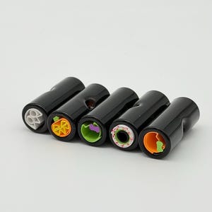 May include: Five cylindrical black beads arranged in a row, each featuring a unique colorful inlay on one end. The designs include a white skull, an orange pumpkin, a green ghost, a white circle with red dots, and an orange crescent shape.