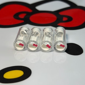 Può includere: Quattro filtri per sigarette in vetro trasparente con un design Hello Kitty bianco e un fiocco rosa.