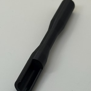 May include: A black, elongated tool with a cylindrical handle and a rectangular opening at one end. The tool has a slightly curved shape and appears to be made of a solid, matte material. The object is set against a plain white background.