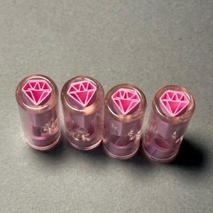 Puede incluir: Cuatro tapones de botella de vidrio rosa con un diseño de diamante rosa en la parte superior.