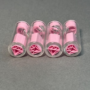 Può includere: Quattro tubi di vetro trasparente con tappi a forma di diamante rosa. I tappi sono realizzati in un materiale morbido e flessibile e hanno una forma di diamante in rilievo.