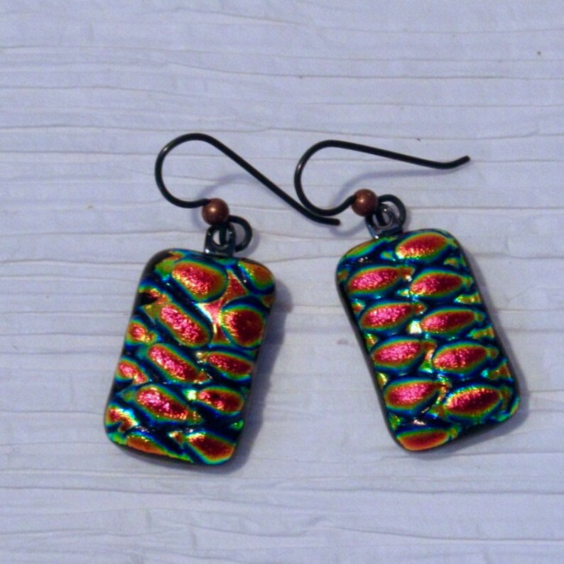 May include: A pair of iridescent glass earrings with a textured, bubble-like design. The earrings are rectangular in shape and have a copper-toned hook.