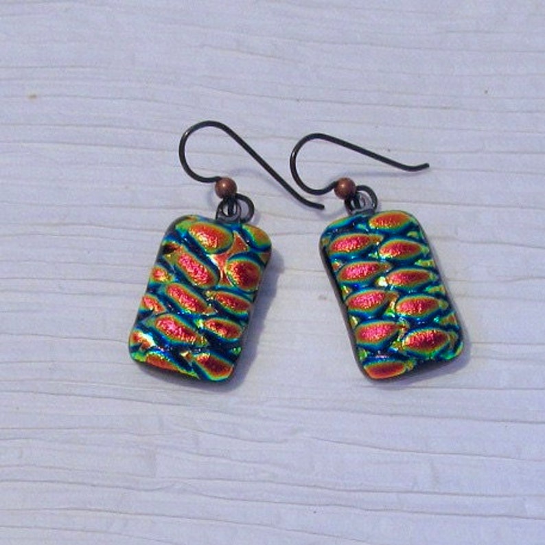 May include: A pair of earrings with a geometric design. The earrings are made of iridescent glass with a blue, green, and red color scheme. The earrings are suspended from silver-toned hooks.