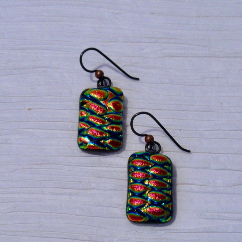 May include: A pair of iridescent glass earrings with a textured pattern. The earrings are rectangular in shape and have a copper-colored hook.