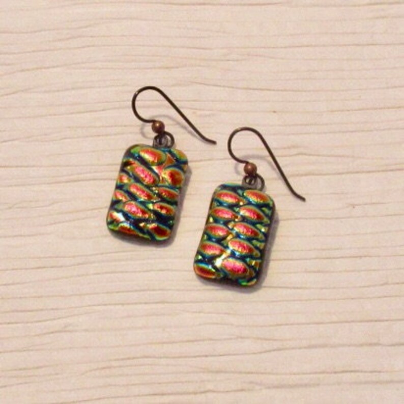 May include: A pair of iridescent earrings with a textured, rectangular design. The earrings are made of glass and have a copper wire hook.