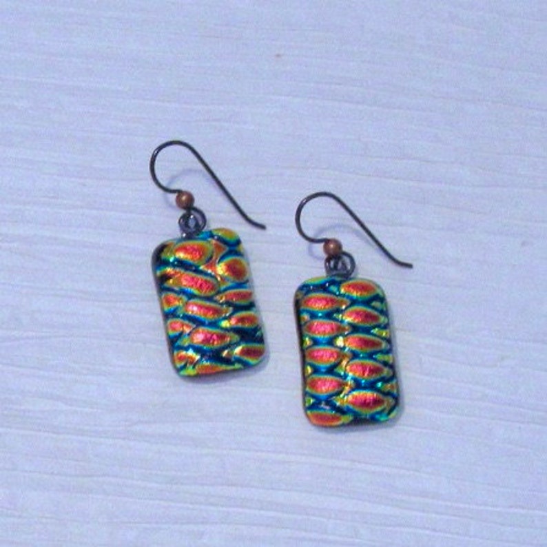 May include: A pair of earrings with a rectangular iridescent glass design. The glass is a mix of blue, green, and orange colors. The earrings are made with silver hooks.
